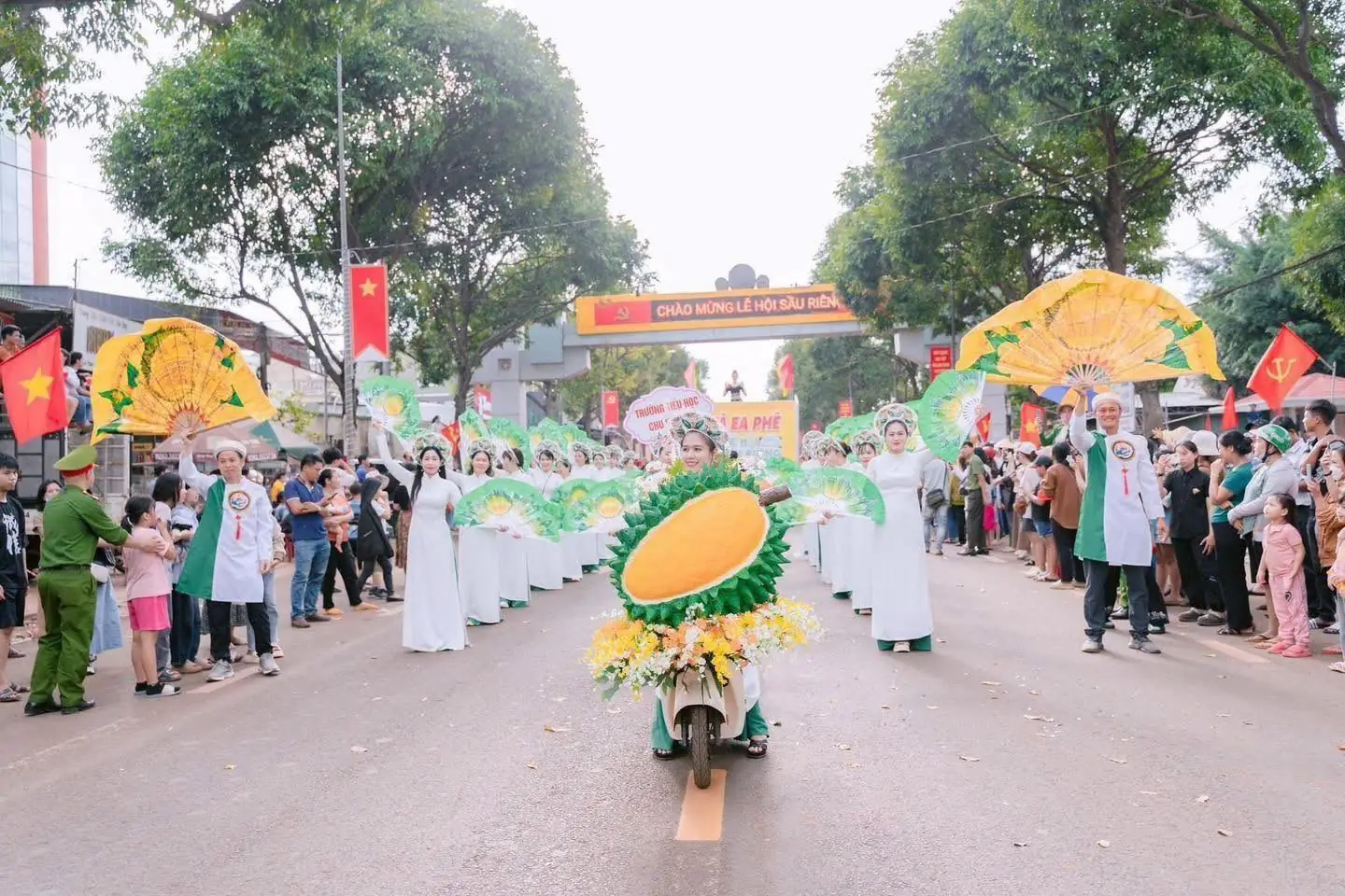 Đoàn diễu hành áo dài cầm quạt đi sau mô hình trái sầu riêng lớn trên đường phố, hai bên đông người xem