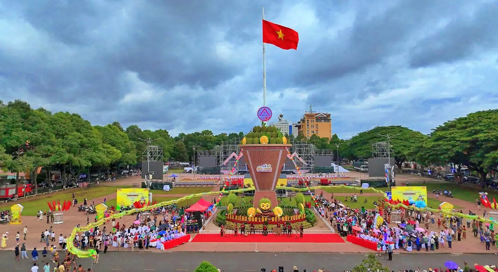 Toàn cảnh quảng trường có cột cờ, sân khấu lớn và mô hình gùi sầu riêng, đông người dự lễ