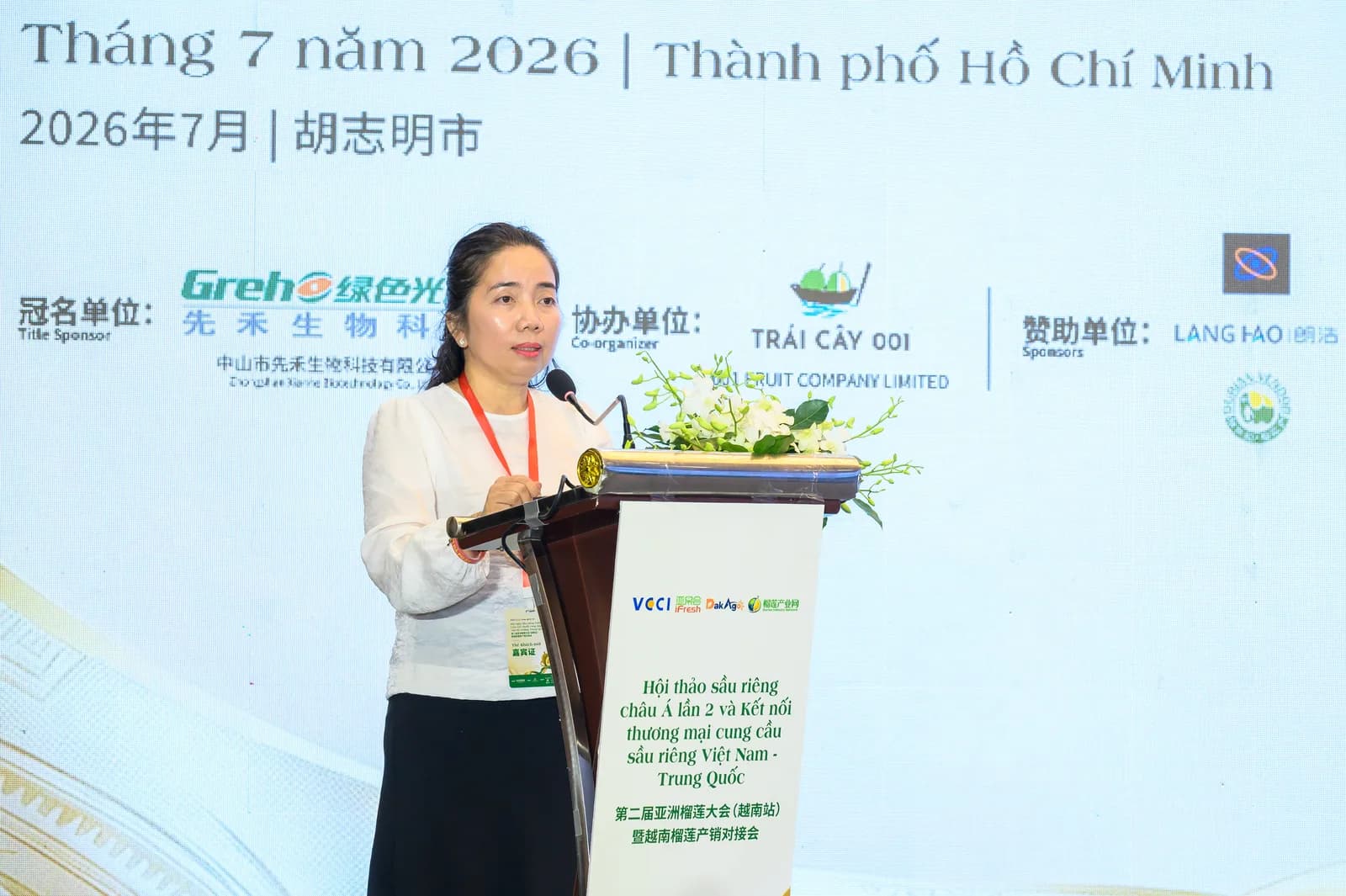 Diễn giả trình bày tham luận trên bục Hội nghị Sầu riêng Châu Á lần thứ 2, phía sau là bảng ghi các đơn vị đồng hành và nhà tài trợ của chương trình
