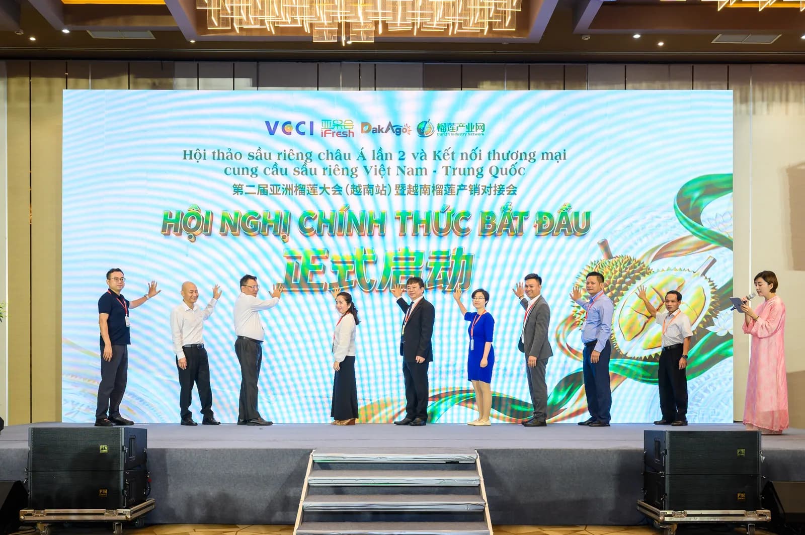 Đại biểu đứng trên sân khấu thực hiện nghi thức khai mạc, màn hình LED phía sau hiện dòng chữ song ngữ Hội nghị chính thức bắt đầu