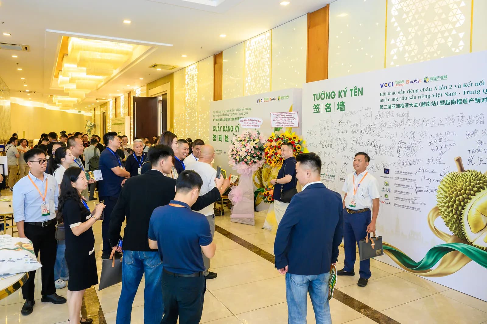 Khu vực đón tiếp với tường ký tên song ngữ Việt – Trung mang logo VCCI, iFresh, DakAgo và quầy đăng ký đại biểu Hội nghị Sầu riêng Châu Á lần thứ 2